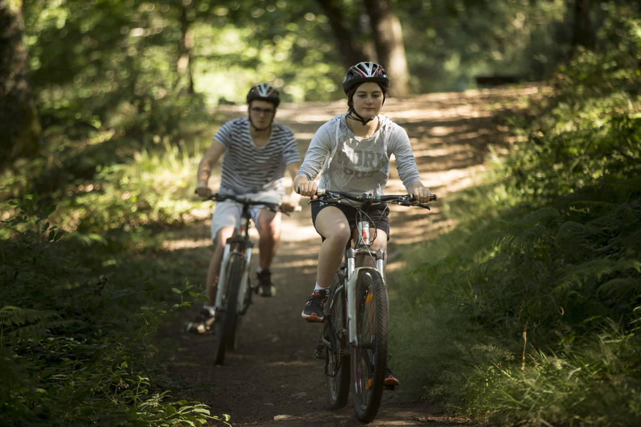 Amis sur le sentier du tour du lac de Guerlédan, à vélo et VTT, traversant la forêt. Crédit : Yannick Derennes